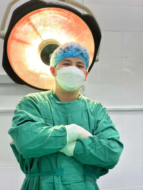 Một bác sĩ của Phòng khám Hiệp Lợi trong trang phục phòng mổ, khoanh tay dưới đèn mổ